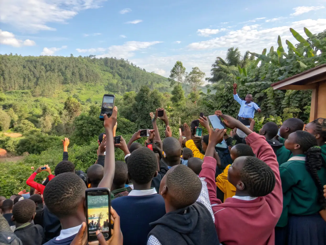 A diverse group of Rwandan students are enthusiastically using the Bakame app on their mobile phones in a rural setting, showcasing the platform's accessibility and engagement.